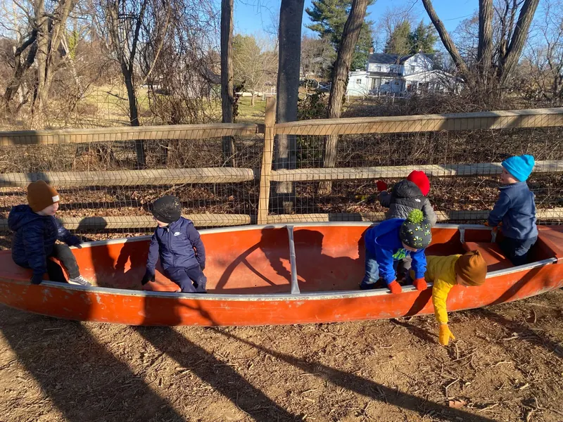 Children in winter hats playing in an old canoe in the play yard