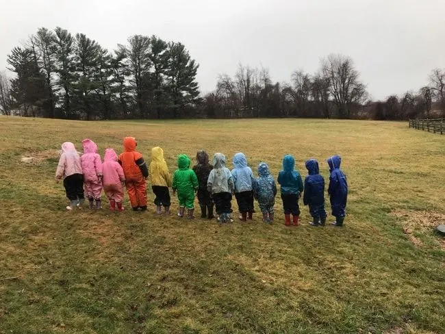 A line of children in rain suits walking across a field